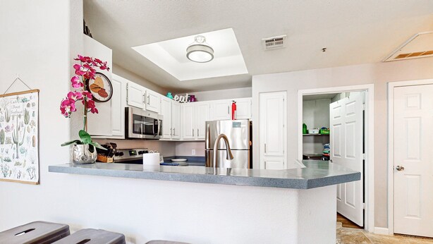 A kitchen with white cabinets, a stainless steel refrigerator, a microwave, and a ceiling light fixture. - Inviting Condo w/ a Shared, Heated Pool, Hot Tub, Fitness Room & Sauna (Scottsdale)