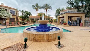 A swimming pool with a central fountain, palm trees, and a covered seating area. - Inviting Condo w/ a Shared, Heated Pool, Hot Tub, Fitness Room & Sauna (Scottsdale)