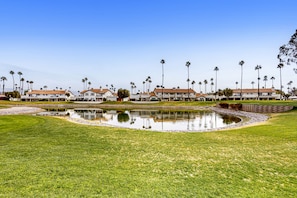 A residential area with a pond, palm trees, and houses with red roofs. - Stunning Condo with Mountain & Golf Course Views - Resort-Style Amenities (Palm Desert)