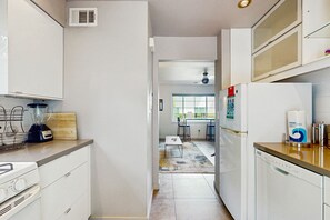 A modern kitchen with white cabinets, a built-in dishwasher, a blender, and a window overlooking a dining area. - Updated modern condo w/ shared pool & mountain views - near downtown (Palm Springs)