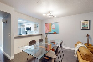 Ein zeitgemäßer Essbereich mit Glastisch, Stühlen, einer Küche im Hintergrund und einem gerahmten Bild an der Wand.