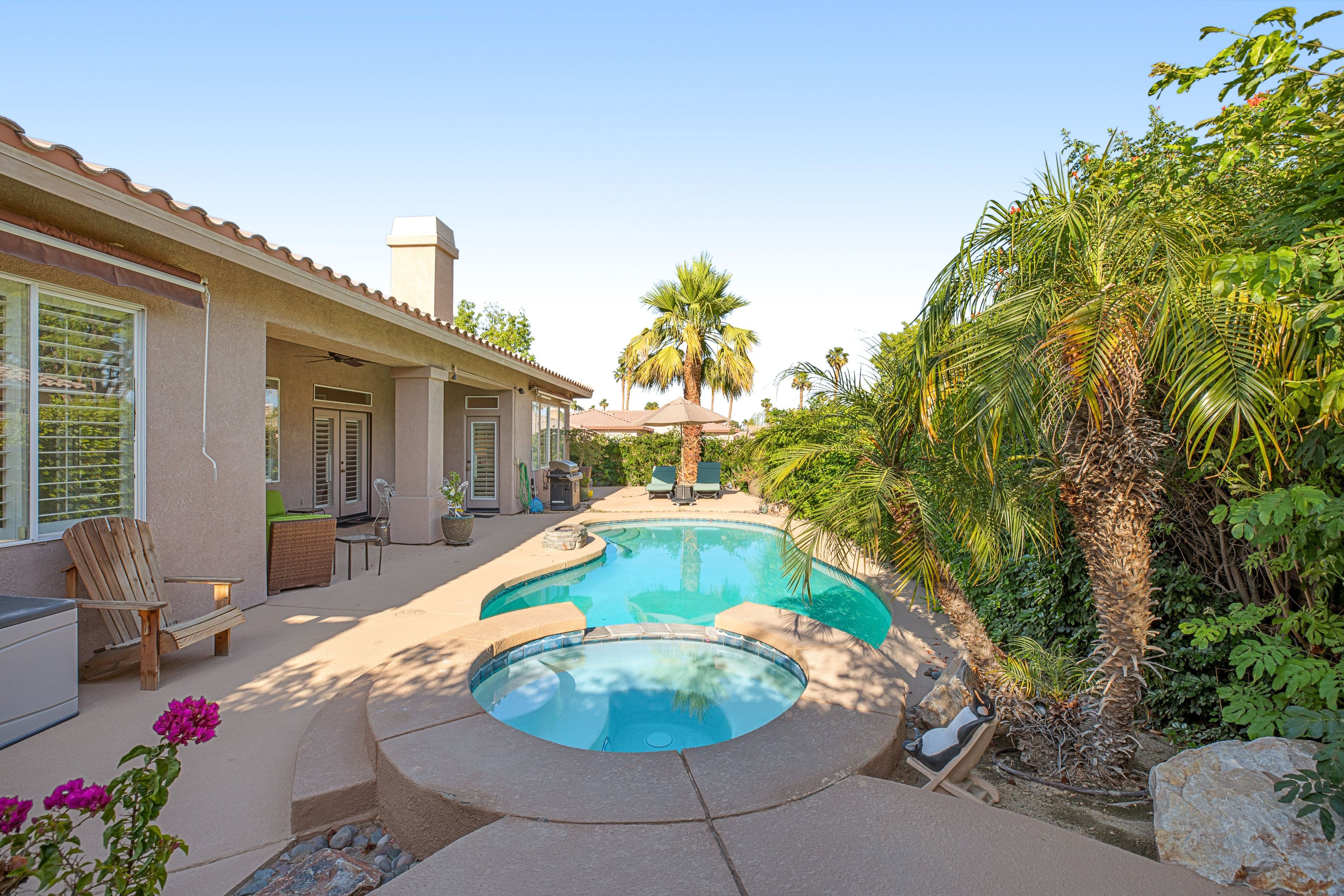 A residential property with a swimming pool, outdoor furniture, and a variety of plants.