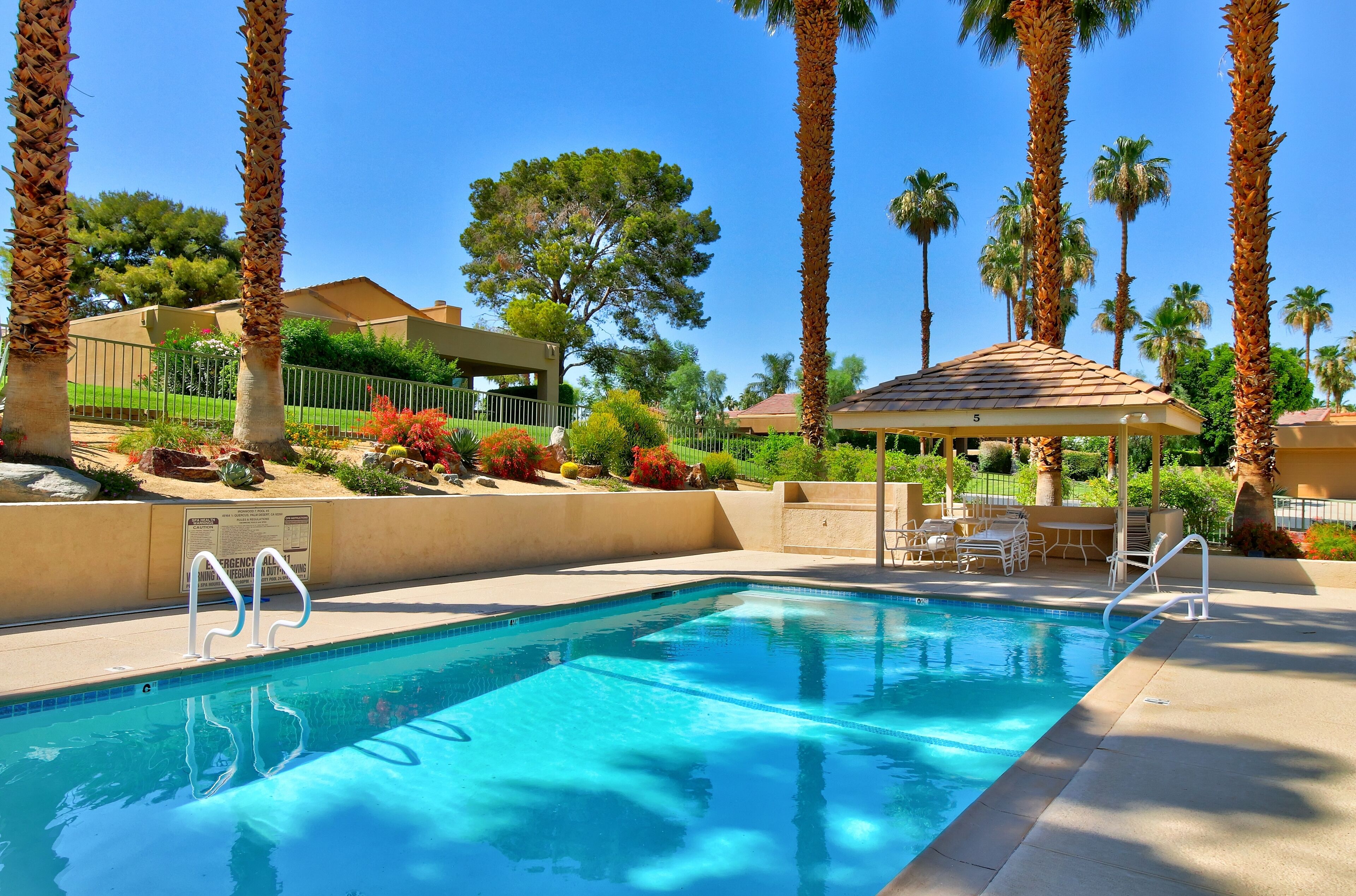 A pool with clear blue water, surrounded by palm trees and a gazebo.