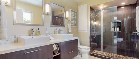 A modern bathroom with dual sinks, a large mirror, a shower enclosure, and a red rug.