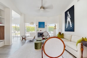 Una sala de estar moderna con un sofá blanco, una silla redonda de madera, un reposapiés verde y un cuadro grande en la pared.