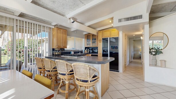 A modern kitchen with a central island, bar stools, and a dining area with a table. - Dog-friendly mountain view condo with pool, grill, open layout, AC, & internet (Palm Desert)