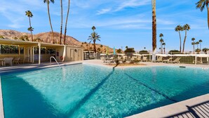 A swimming pool with clear blue water, surrounded by palm trees and a desert landscape in the background. - Dog-friendly mountain view condo with pool, grill, open layout, AC, & internet (Palm Desert)