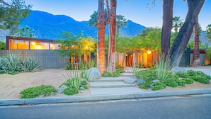 A modern house with a large window, a stone wall, and a well-maintained garden with various plants and rocks. - Elegant, mid-century Alexander butterfly home w/ pool & gas grill (Palm Springs)