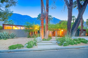 A modern house with a large window, a stone wall, and a well-maintained garden with various plants and rocks.