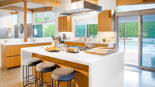 A modern kitchen with a large island, wooden cabinets, and a view of a backyard. - Elegant, mid-century Alexander butterfly home w/ pool & gas grill (Palm Springs)