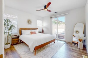 Un dormitorio con una cama de madera, un ventilador de techo, un espejo grande y una planta en maceta.