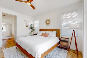A bedroom with a wooden bed, white bedding, a ceiling fan, a sunburst wall decoration, a potted plant, and a tripod lamp. - Serene home with pool spa, gas fireplace, AC, pool and golf access - dogs ok (Indio)