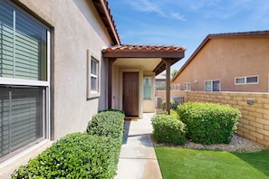 A residential building with a covered entrance, a door, and a small front yard with neatly trimmed bushes. - Serene home with pool spa, gas fireplace, AC, pool and golf access - dogs ok (Indio)