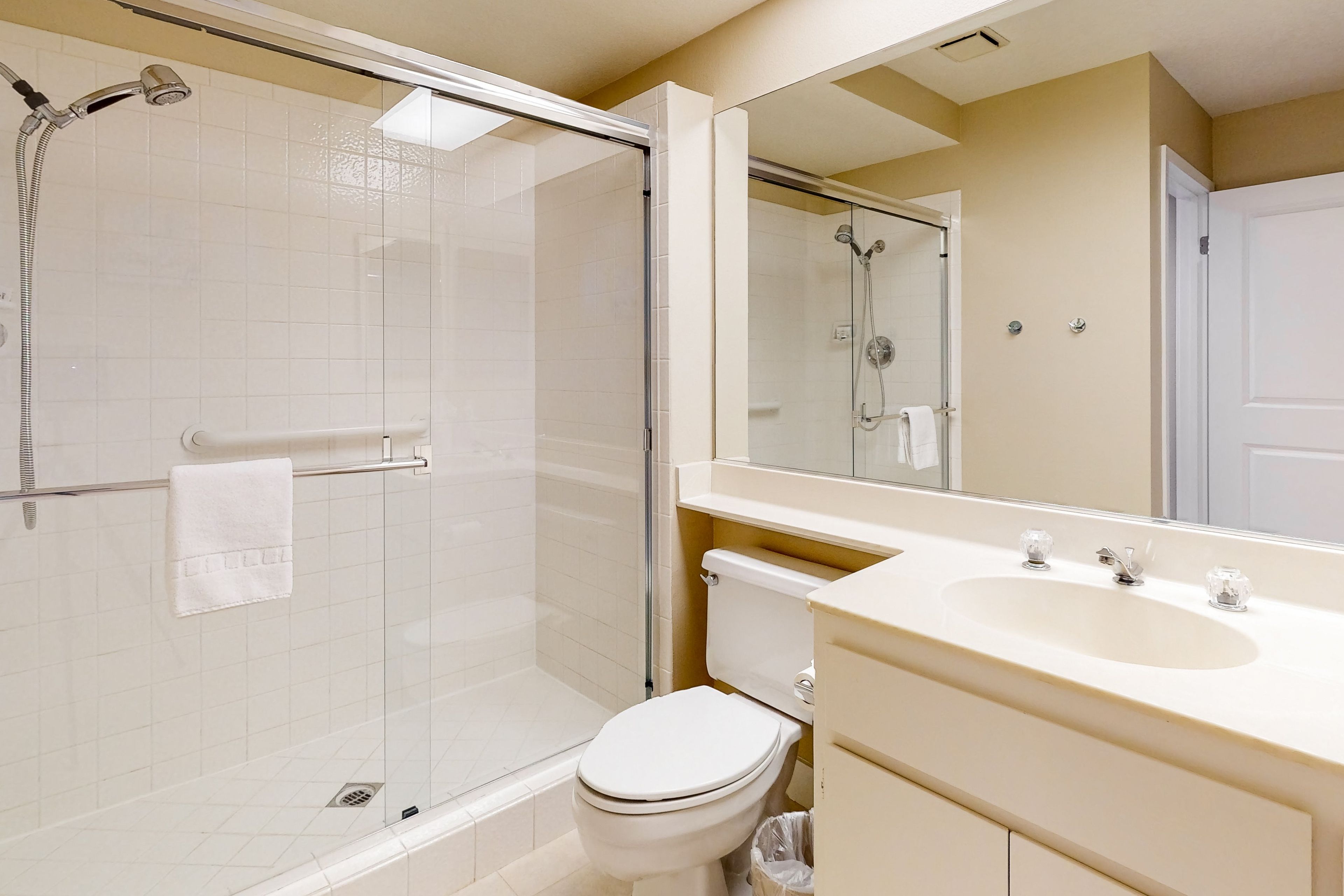 A bathroom with a glass-enclosed shower, a toilet, and a sink with a mirror above it.