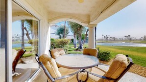 Une terrasse couverte avec une table ronde et quatre chaises, donnant sur un terrain de golf et un plan d’eau.