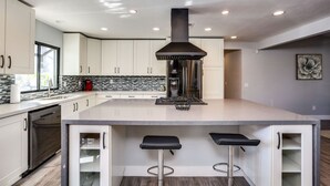 Cozinha moderna com armários brancos, uma ilha central com banquetas, coifa de aço inoxidável e backsplash com padrão de mosaico.