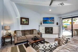A living room with a sofa set, a coffee table, a fireplace, and a TV mounted on the wall. - Dog-friendly desert gem w/private pool, putting green, firepit, & more (Palm Springs)