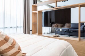 Quarto de hotel com uma cama grande, televisão, sofá e uma mesinha.
