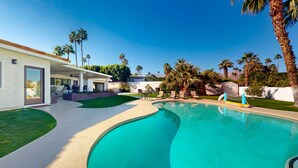 Ein modernes Haus mit Swimmingpool, Palmen und blauem Himmel.