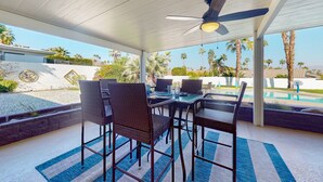 Eine Terrasse im Freien mit Deckenventilator, Pool und Essbereich mit Stühlen und Tischen.