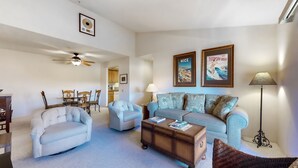 A living room with a sofa, armchair, coffee table, and floor lamp. There are framed pictures on the wall and a ceiling fan. - Dog-friendly condo w/ two shared outdoor pools, spas & tennis court (Palm Springs)