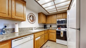 A kitchen with wooden cabinets, a microwave, an oven, a refrigerator, a sink, and a decorative wall clock. - Dog-friendly condo w/ two shared outdoor pools, spas & tennis court (Palm Springs)