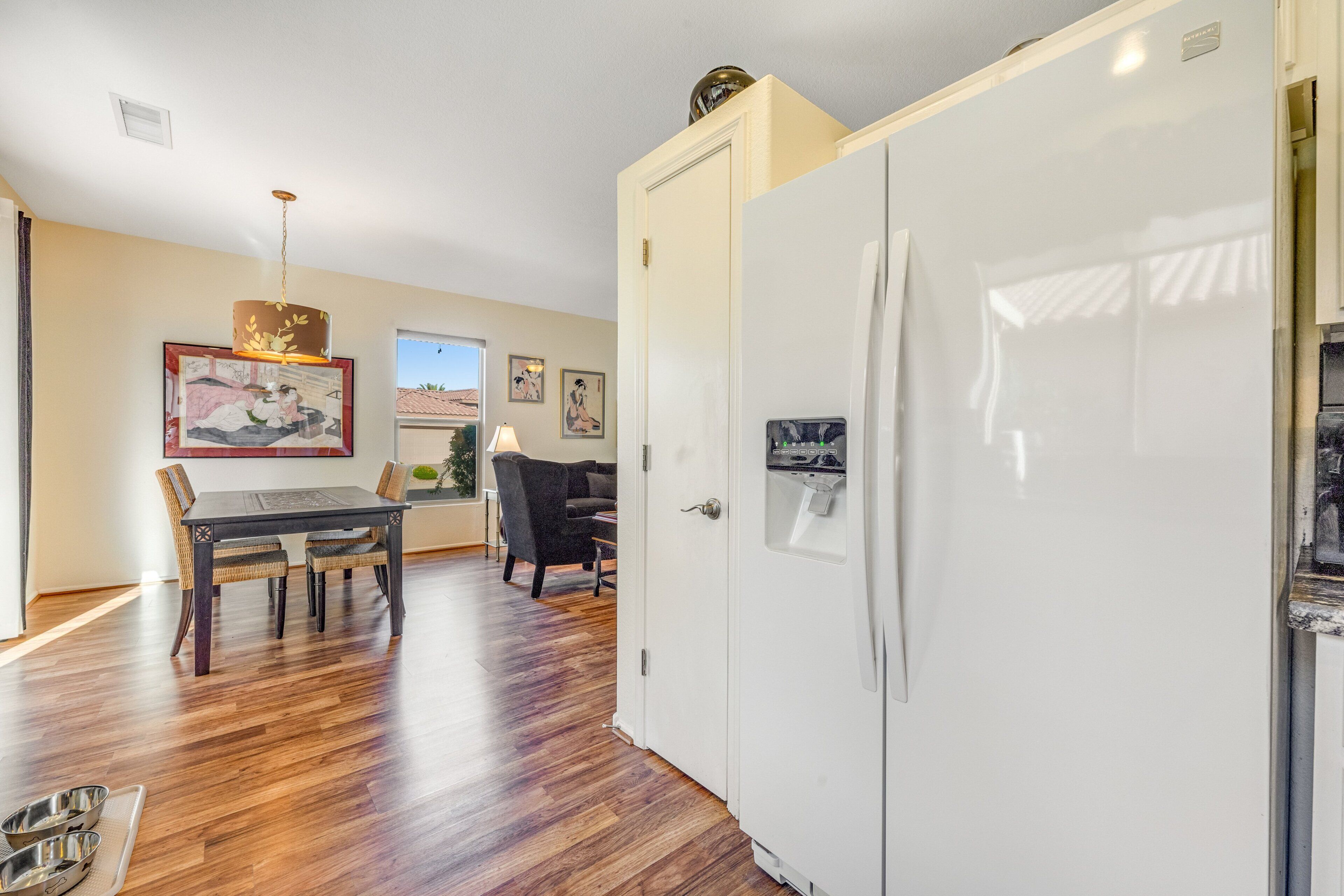 A modern kitchen with a white refrigerator, wooden flooring, and a dining area with a table and chairs.