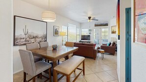 A dining area with a wooden table and chairs, a ceiling fan, and a TV in the background.