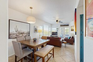 Ein Essbereich mit Holztisch und -stühlen, einem Deckenventilator und einem Fernseher im Hintergrund.