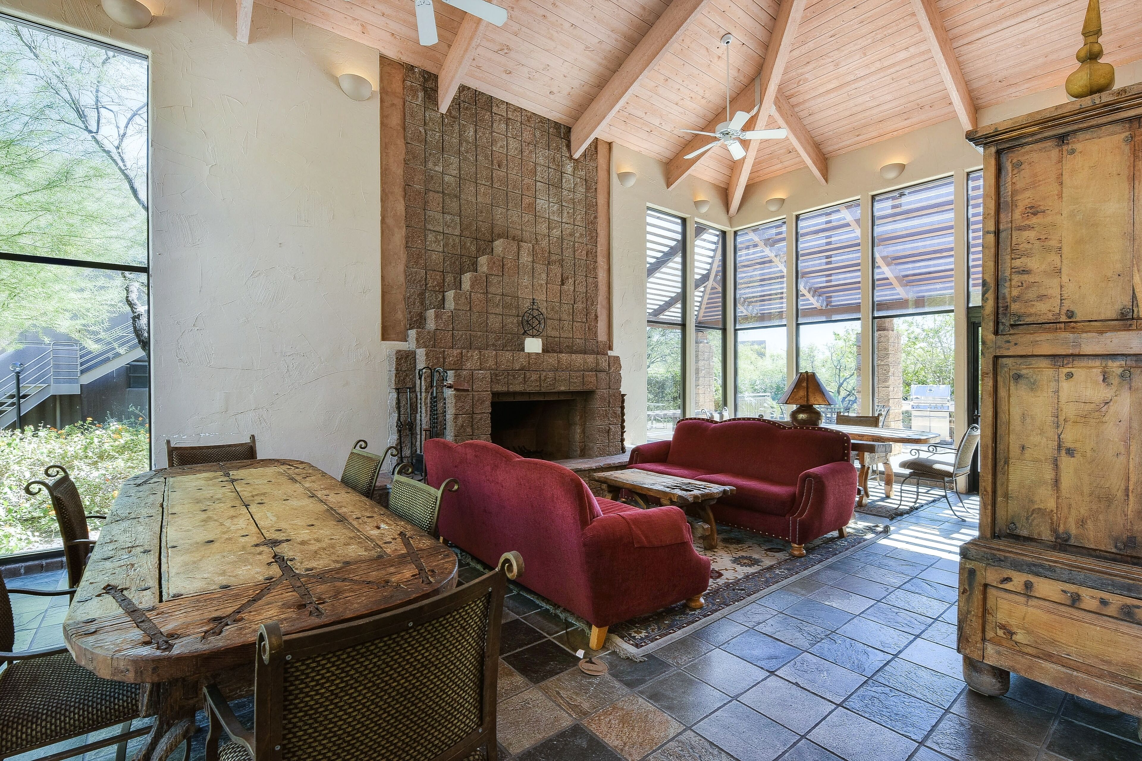 A rustic interior with a stone fireplace, wooden ceiling beams, and large windows.