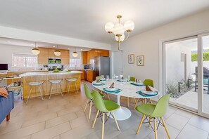 Cozinha moderna com área de jantar, apresentando uma ilha grande, cadeiras verdes e um lustre.