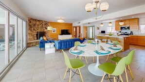 Una sala de estar moderna con pared de piedra, un sofá azul y un comedor con sillas verdes y una mesa blanca.