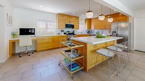 Una cocina moderna con armarios de madera, una isla central, taburetes de bar y un carro con cristalería.