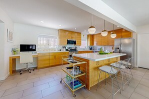 A modern kitchen with wooden cabinets, a central island, bar stools, and a cart with glassware. - Classic, mid-century modern home w/ mtn views, private pool and spa - dogs OK (Palm Springs)