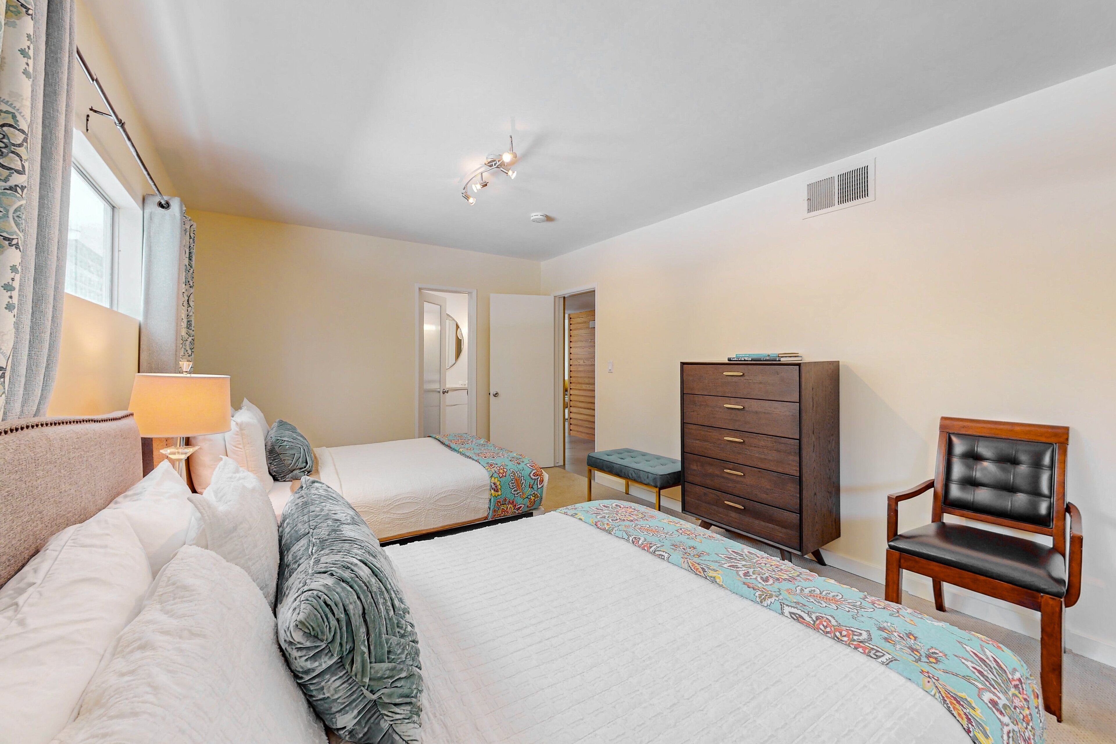 A bedroom with two beds, a dresser, a chair, and a lamp.
