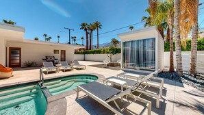 Un área de piscina moderna al aire libre con sillones de descanso, un jacuzzi y palmeras.