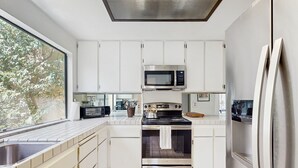 A modern kitchen with white cabinets, a stainless steel oven, a microwave, and a refrigerator. - Stay Awhile: Enjoy Relaxed, Comfortable Living in the Heart of Palm Desert. (Palm Desert)
