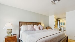 A bedroom with a large bed, a nightstand with a lamp, a dresser, and a mirror. - Stay Awhile: Enjoy Relaxed, Comfortable Living in the Heart of Palm Desert. (Palm Desert)