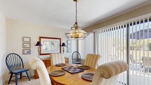 A dining area with a wooden table, six chairs, and a hanging light fixture. - Stay Awhile: Enjoy Relaxed, Comfortable Living in the Heart of Palm Desert. (Palm Desert)
