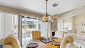 A dining area with a wooden table, four chairs, and a hanging light fixture. - Stay Awhile: Enjoy Relaxed, Comfortable Living in the Heart of Palm Desert. (Palm Desert)