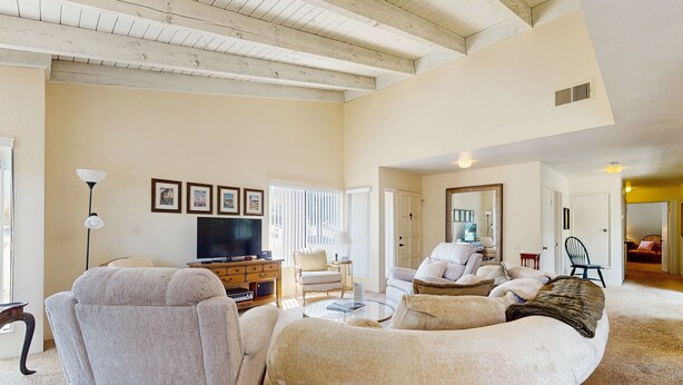 A spacious living room with a high ceiling and exposed beams, a comfortable sofa set, a television, and a dining area with a table and chairs. - Stay Awhile: Enjoy Relaxed, Comfortable Living in the Heart of Palm Desert. (Palm Desert)