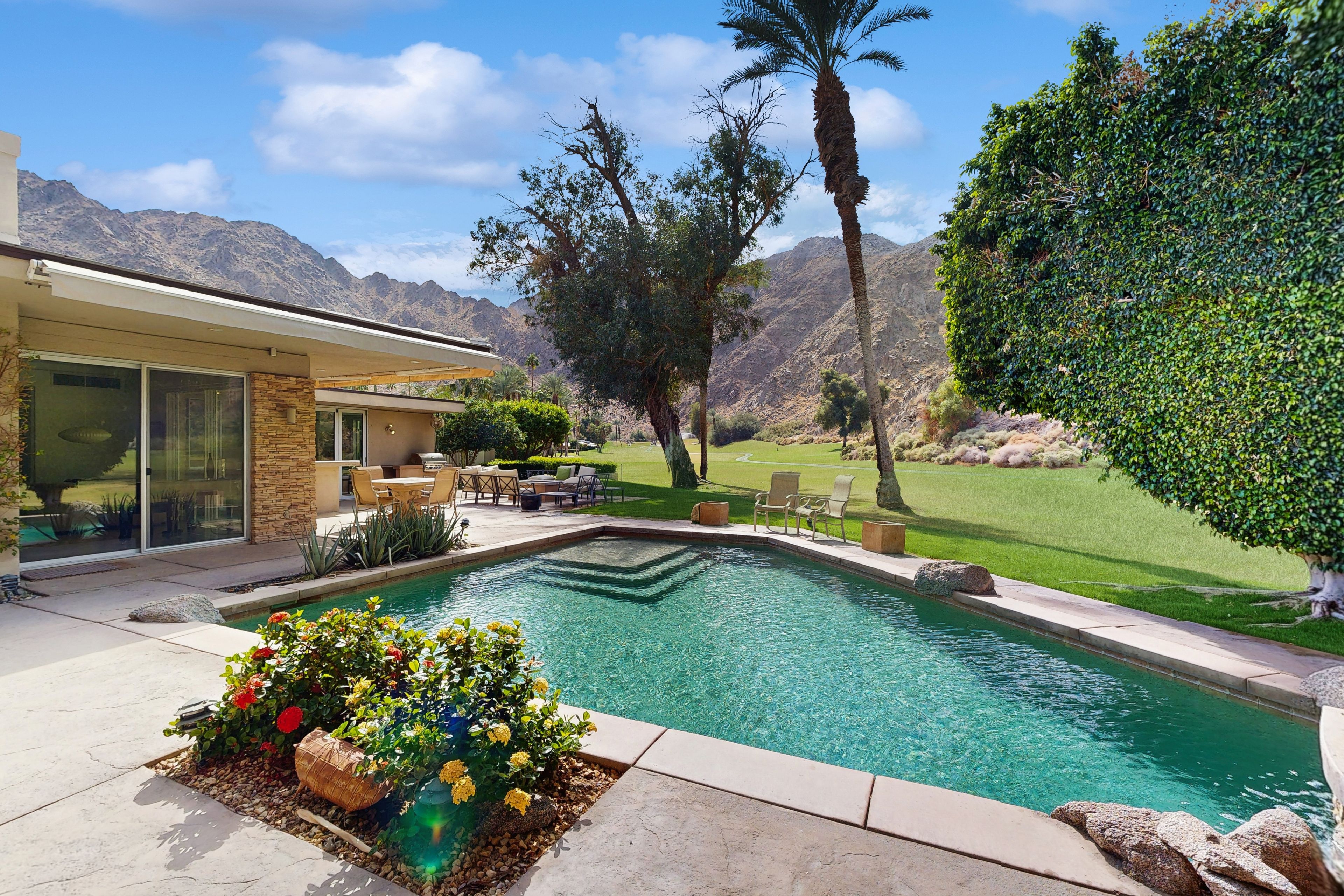 A swimming pool with a stone border, surrounded by a patio area with outdoor furniture.