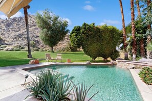 A swimming pool with a clear blue water, surrounded by a well-maintained lawn, a few trees, and a mountain in the background. - Exquisite retreat with pool, spa, fireplace, golf & mountain view, dog-friendly! (Indian Wells)