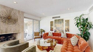 A modern living room with a fireplace, a sectional sofa, a glass coffee table, and a large plant. - Exquisite retreat with pool, spa, fireplace, golf & mountain view, dog-friendly! (Indian Wells)