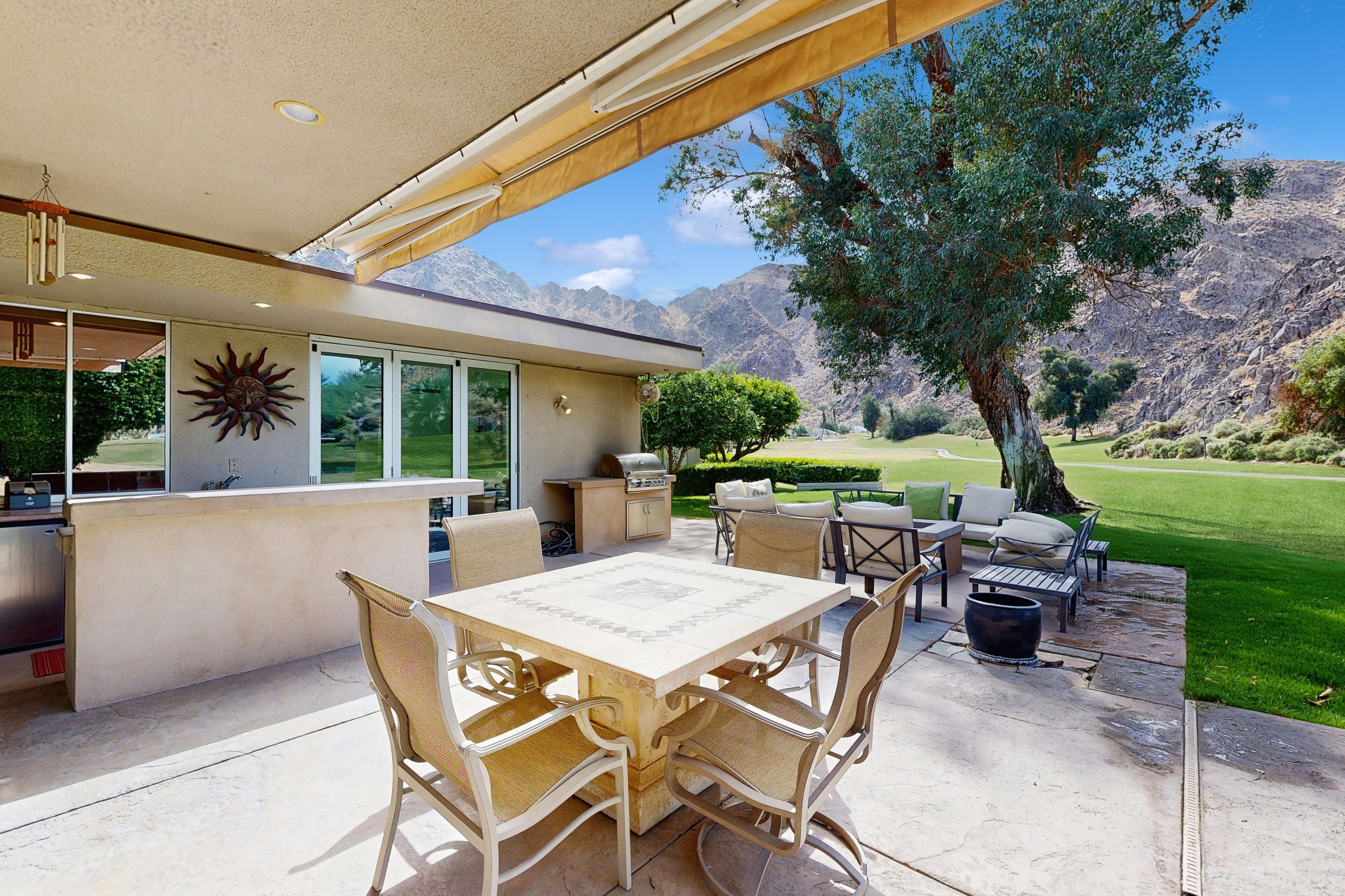 A patio with a table and chairs, a grill, and a view of a mountain landscape.