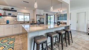 Een moderne keuken met een groot eiland, barkrukken en hanglampen.