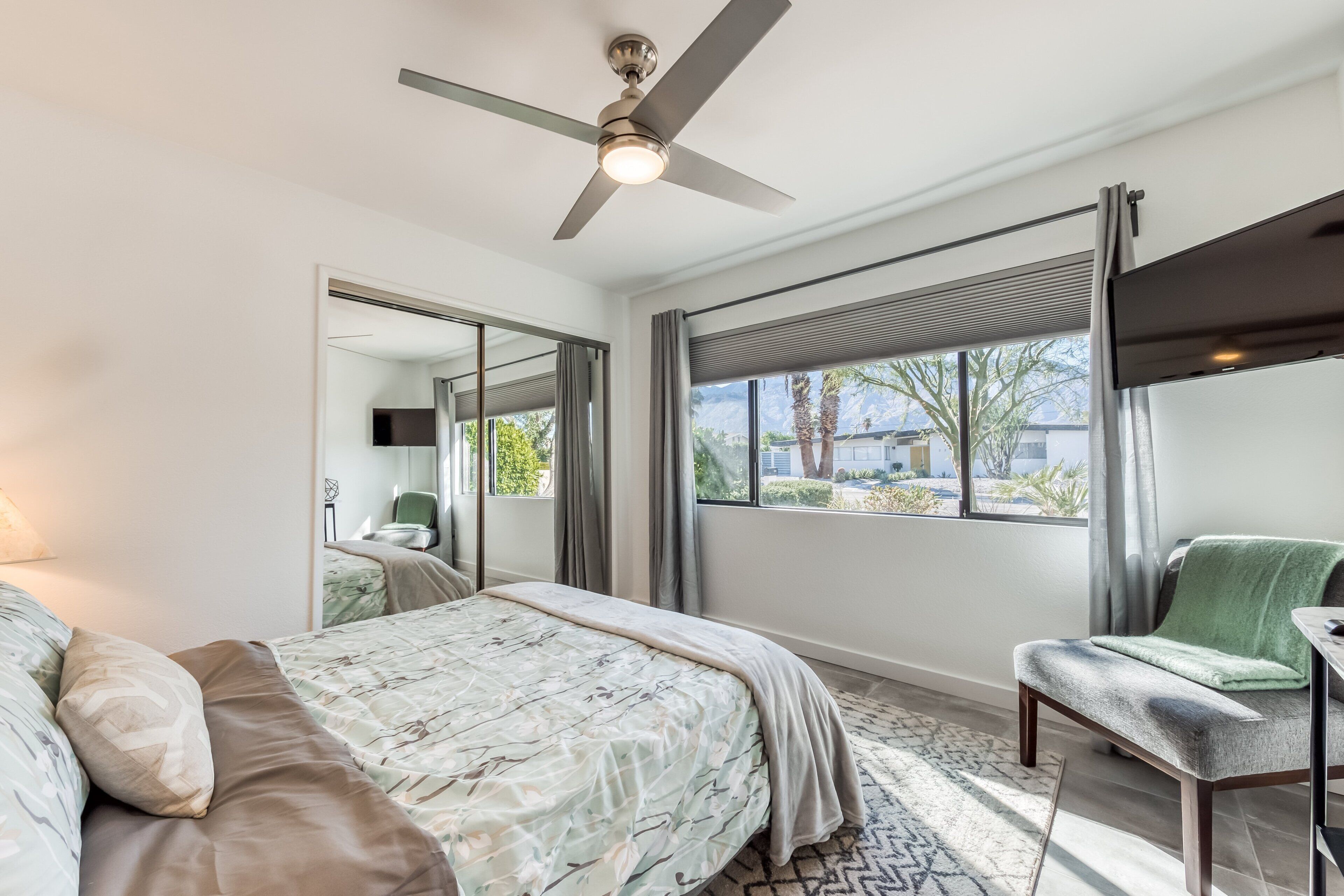 Une chambre à coucher comprenant un lit, une chaise, un ventilateur de plafond, une fenêtre avec vue et un miroir.