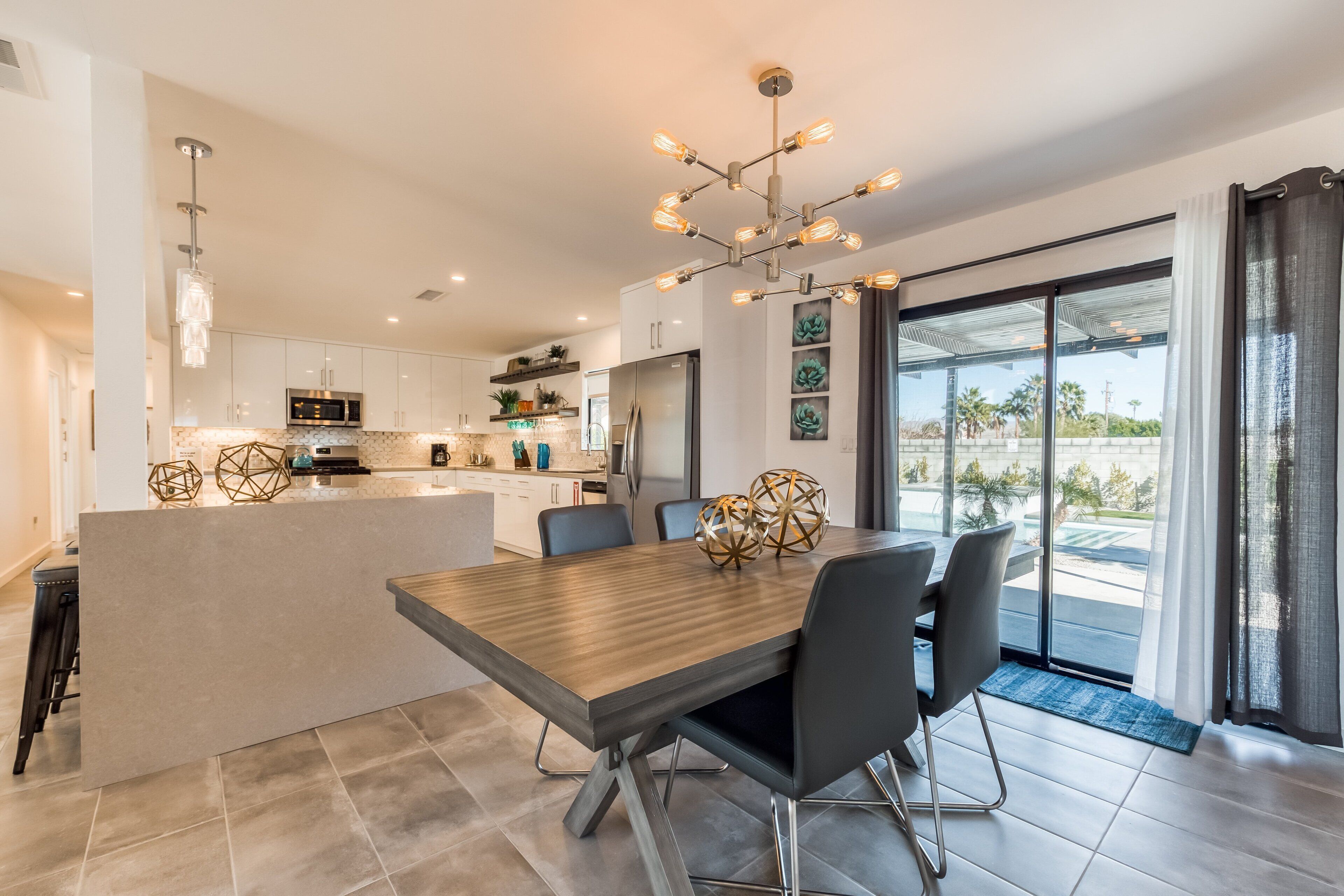 A modern kitchen with a central island, a dining area with a wooden table, and a large sliding glass door leading to a balcony.
