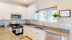A modern kitchen with white cabinets, stainless steel appliances, granite countertops, and hanging plants. - Two-story mountain view retreat with two primary suites & ideal layout (Flagstaff)