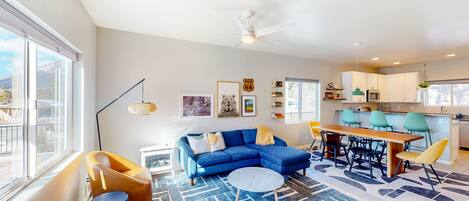 A modern living room with a blue sofa, a round coffee table, and a dining area with a wooden table and chairs.